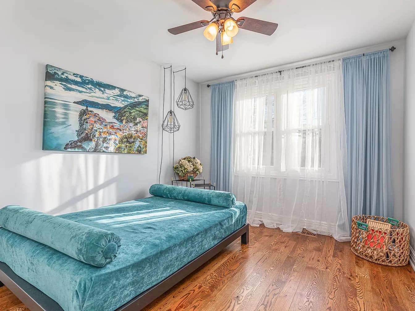 Staged guest bedroom with a teal velvet daybed, layered drapes, and a large seaside canvas